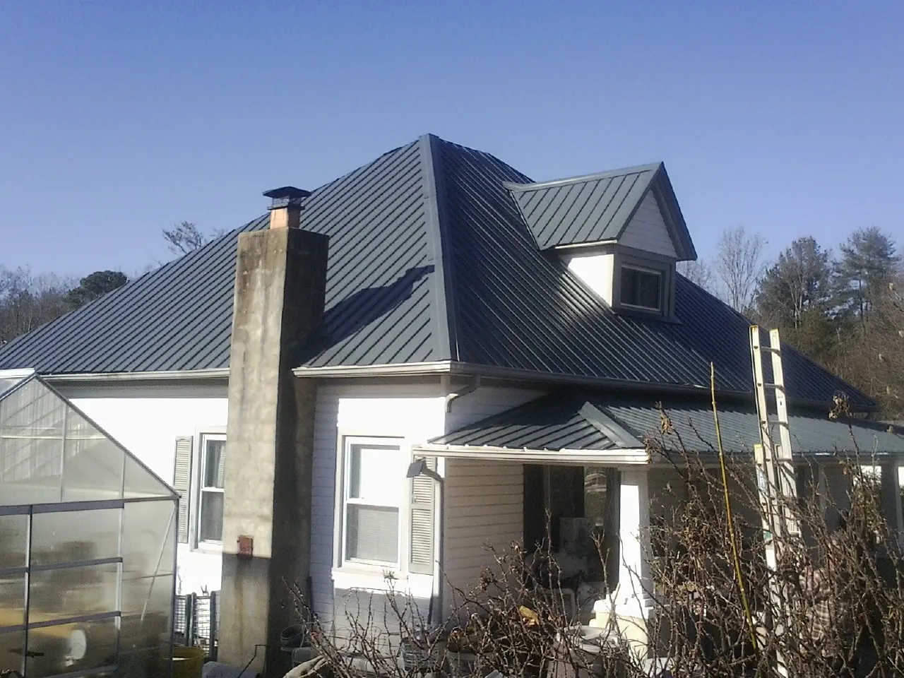 Dark blue standing seam metal roof on a white farmhouse with dormer — Slate & Tile Roof Repair by Roofing Brothers in Fountainville