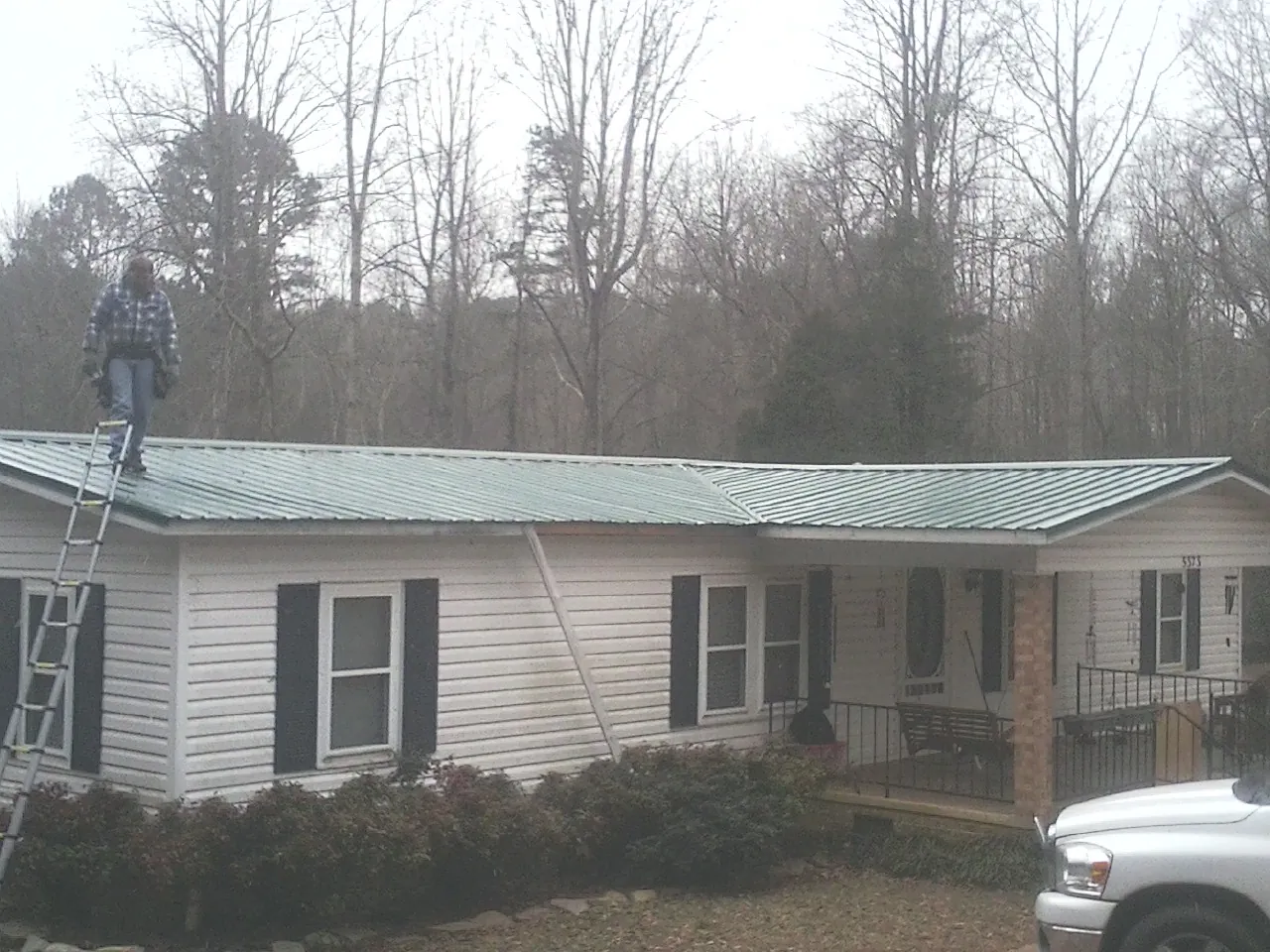 Worker on a ladder beside a new green metal roof on a ranch home in Fountainville
