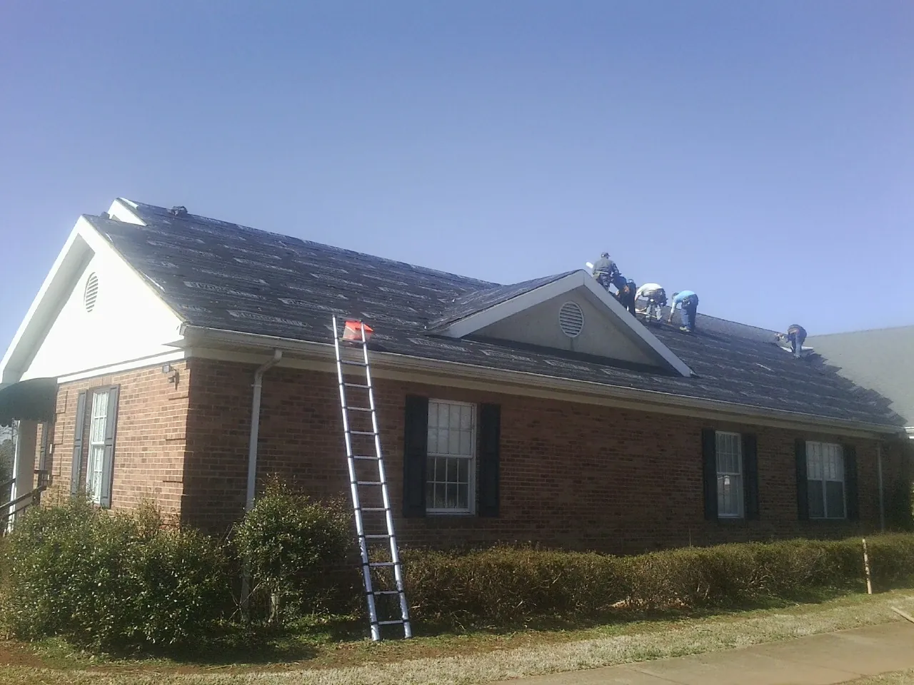 Crew tearing shingles off a brick ranch roof with a ladder set — Metal Roof Repair work by our crew in Fountainville