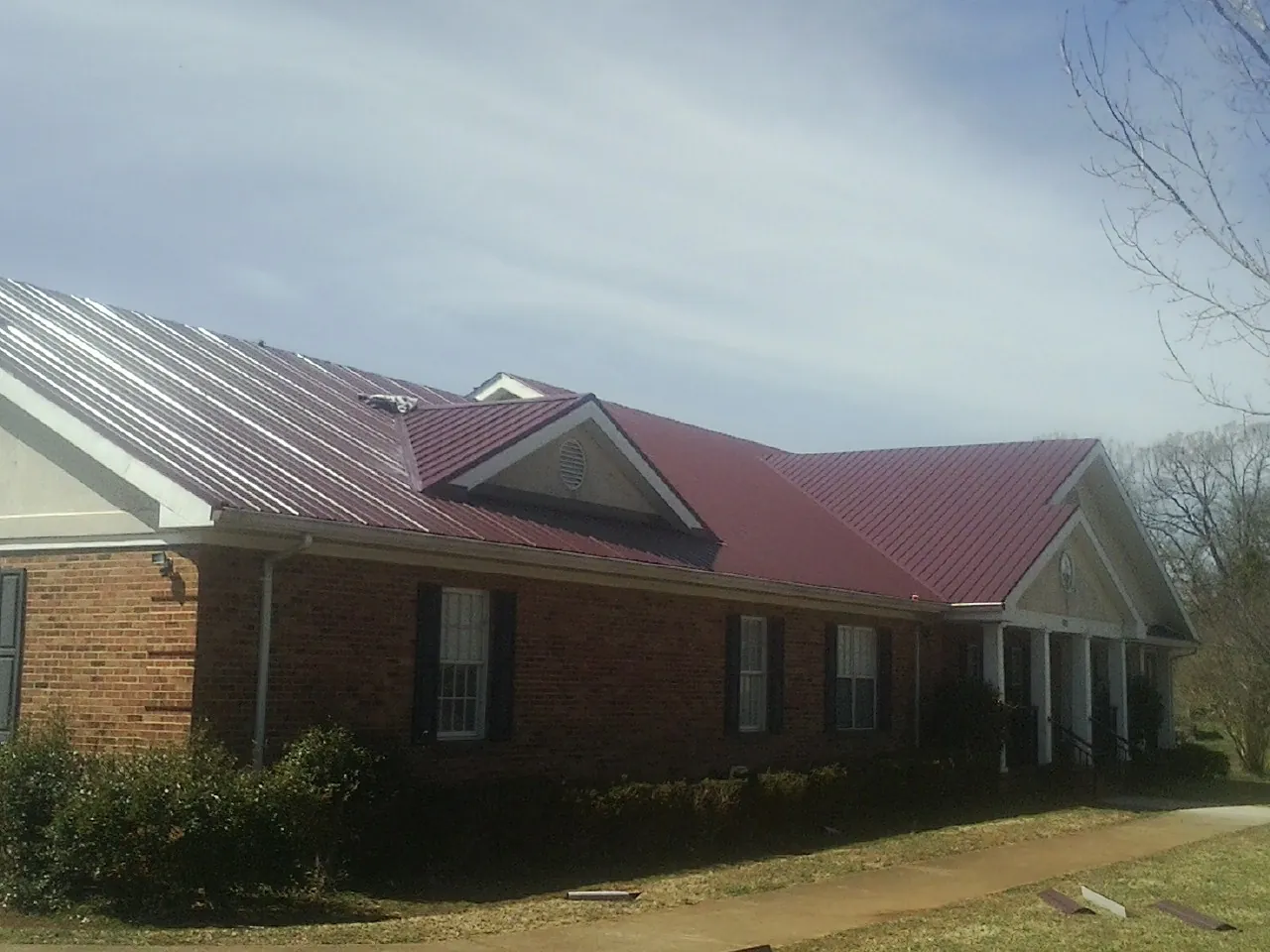 Red metal roof with gabled entries on a long brick building, from a Hail Damage Roof Repair job in Fountainville