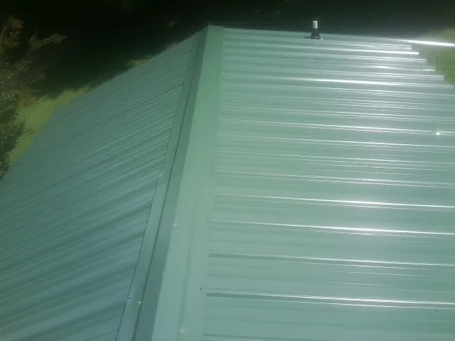 New green metal panels meeting at the ridge of a roof — Flat Roof Repair work by our crew in Fountainville