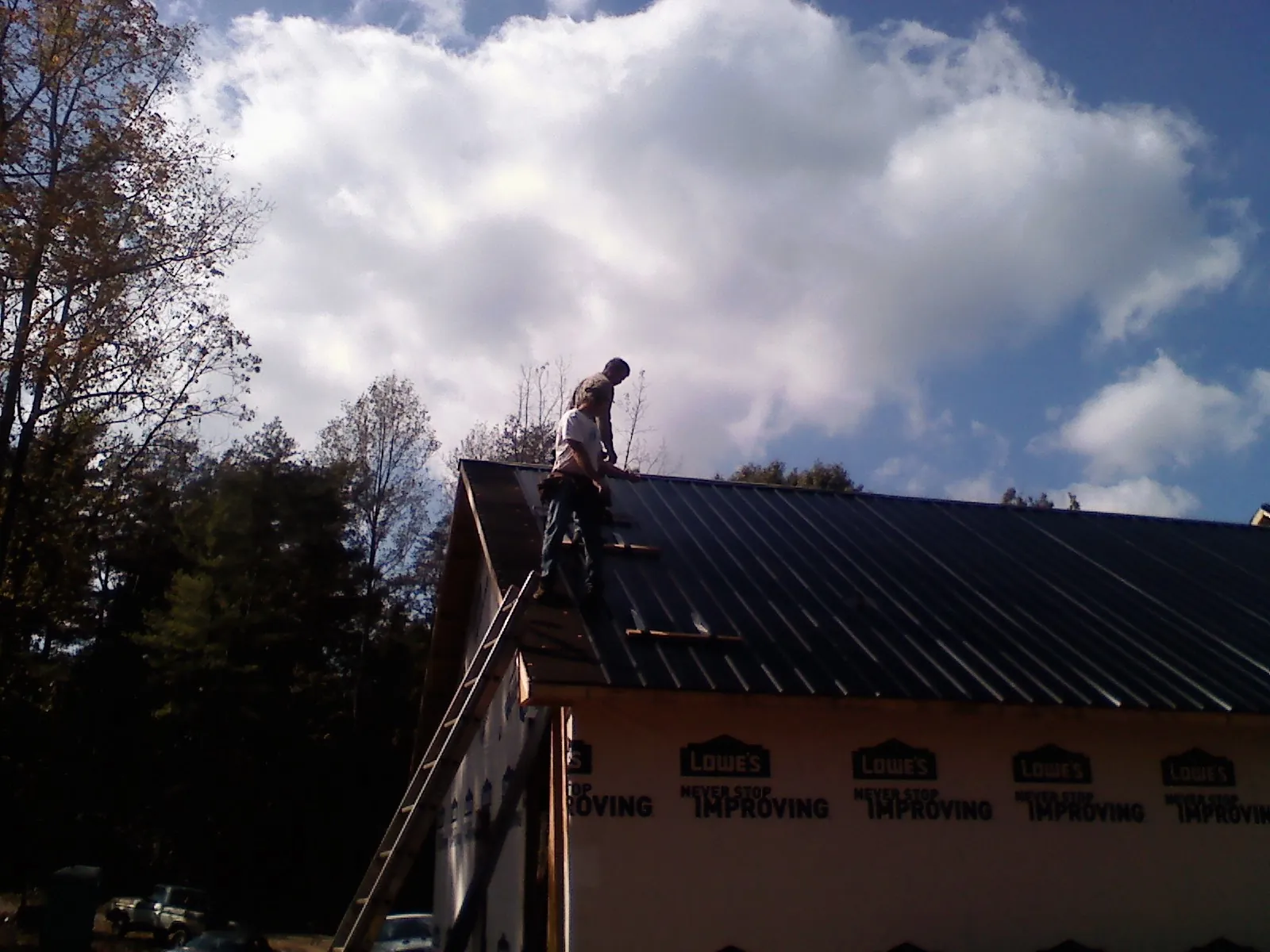 Roofer fastening dark metal panels high against a cloudy sky, from a Roof Inspection job in Fountainville