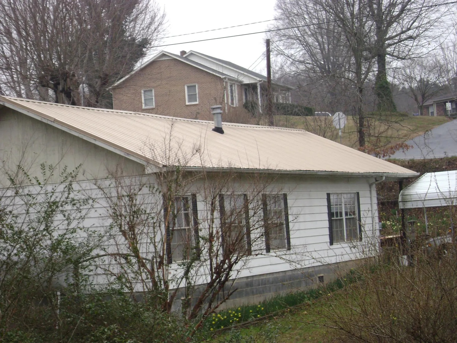 Tan metal roof on a white sided house set into a hillside — Commercial Roofing by Roofing Brothers in Fountainville